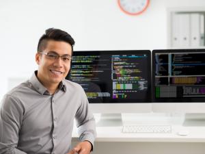 Photo of young adult male sitting in front of computer monitors by Dragon Images, courtesy Getty Images.